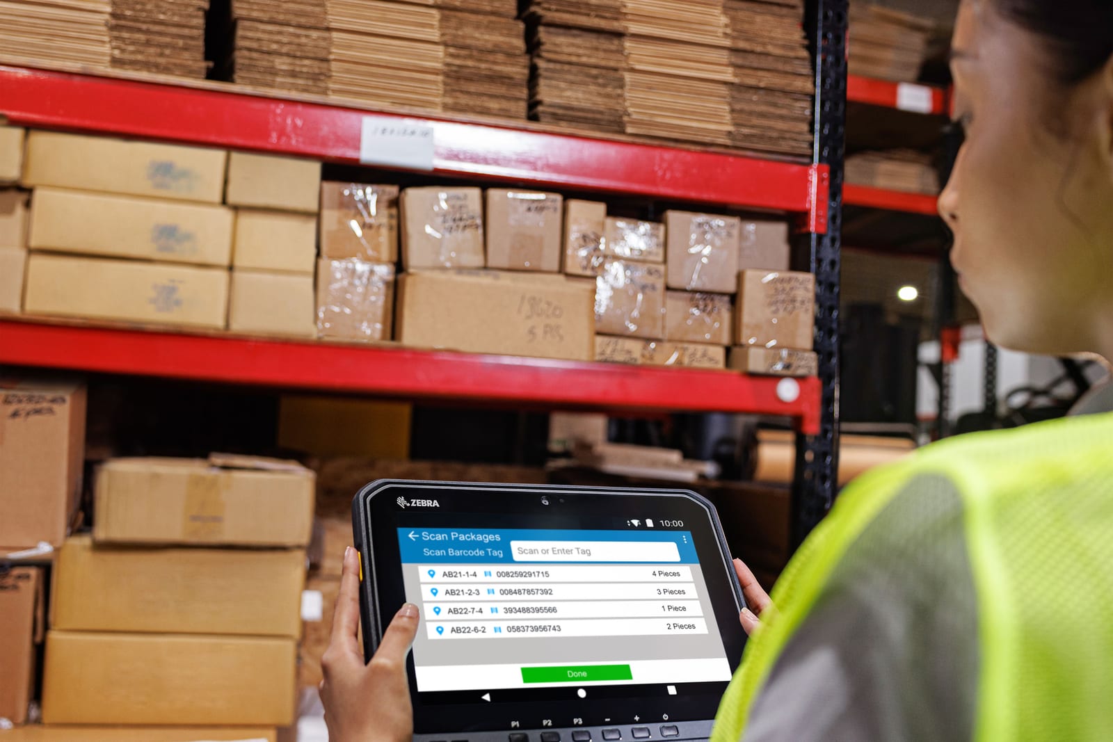 Pracownica magazynu trzyma tablet Zebra ET60 z listą skanowanych paczek, stojąc przy regale z kartonami