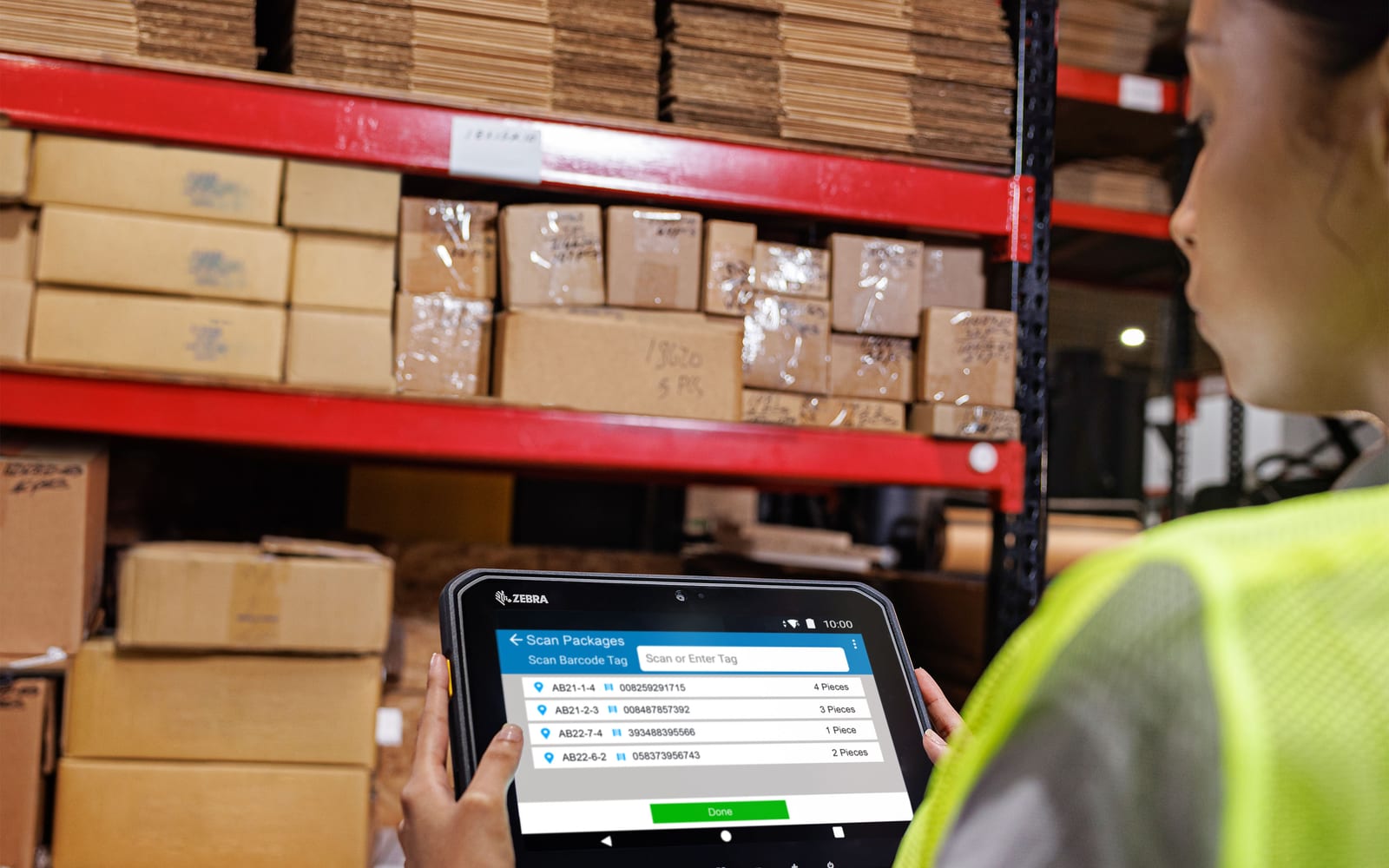 Pracownica magazynu trzyma tablet Zebra ET60 z listą skanowanych paczek przy regale z kartonami