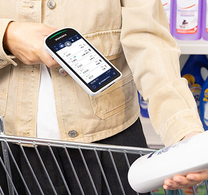 Klientka skanuje towar urządzeniem Datalogic Joya Smart przy regale w sklepie, drugą ręką trzymając wózek