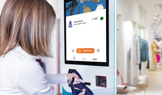 Klientka przy kiosku samoobsługowym w sklepie odzieżowym przykłada metkę ubrania do wbudowanego skanera Datalogic