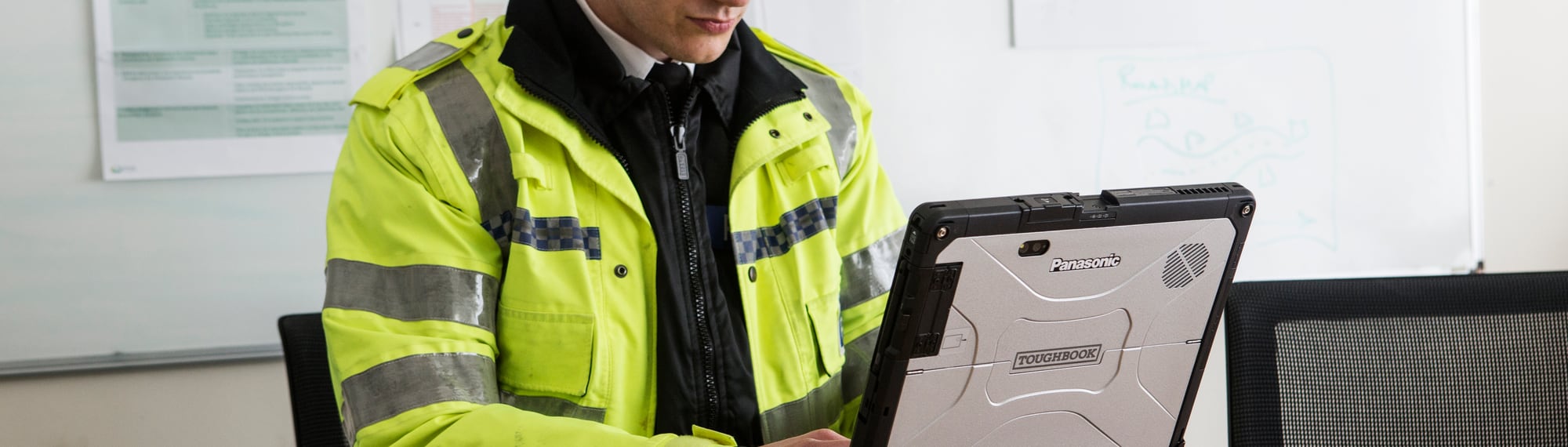 Policjant w kamizelce odblaskowej pracuje na wzmocnionym tablecie 2-w-1 Panasonic TOUGHBOOK 33 opartym o radiowóz