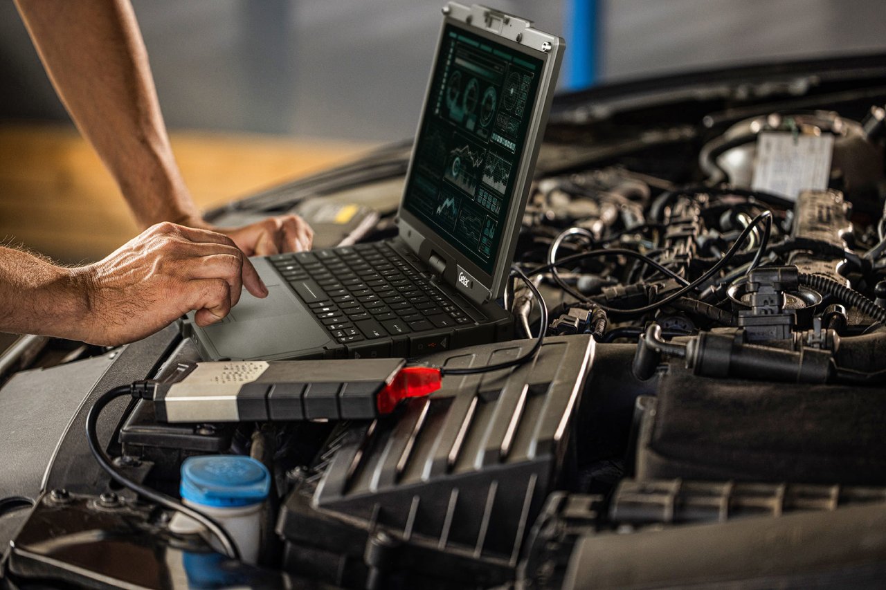 Mechanik pracuje na wzmocnionym laptopie Getac V120 postawionym na silniku samochodu, z podłączonym interfejsem diagnostycznym